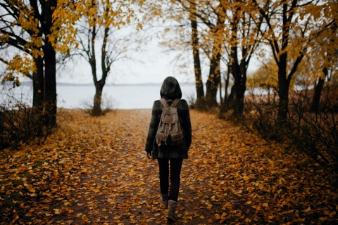 Person with a backpack walking on leaves toward a body of water