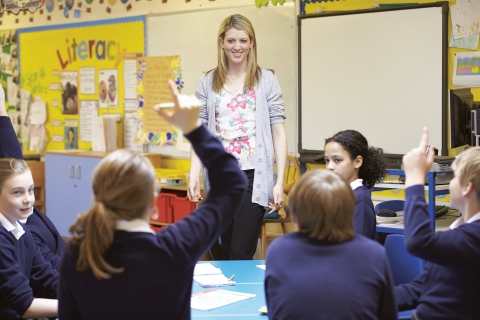 Students raising their hand and teacher smiling in classroom