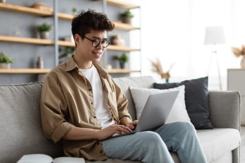 Person sitting on a couch typing on a laptop on their lap