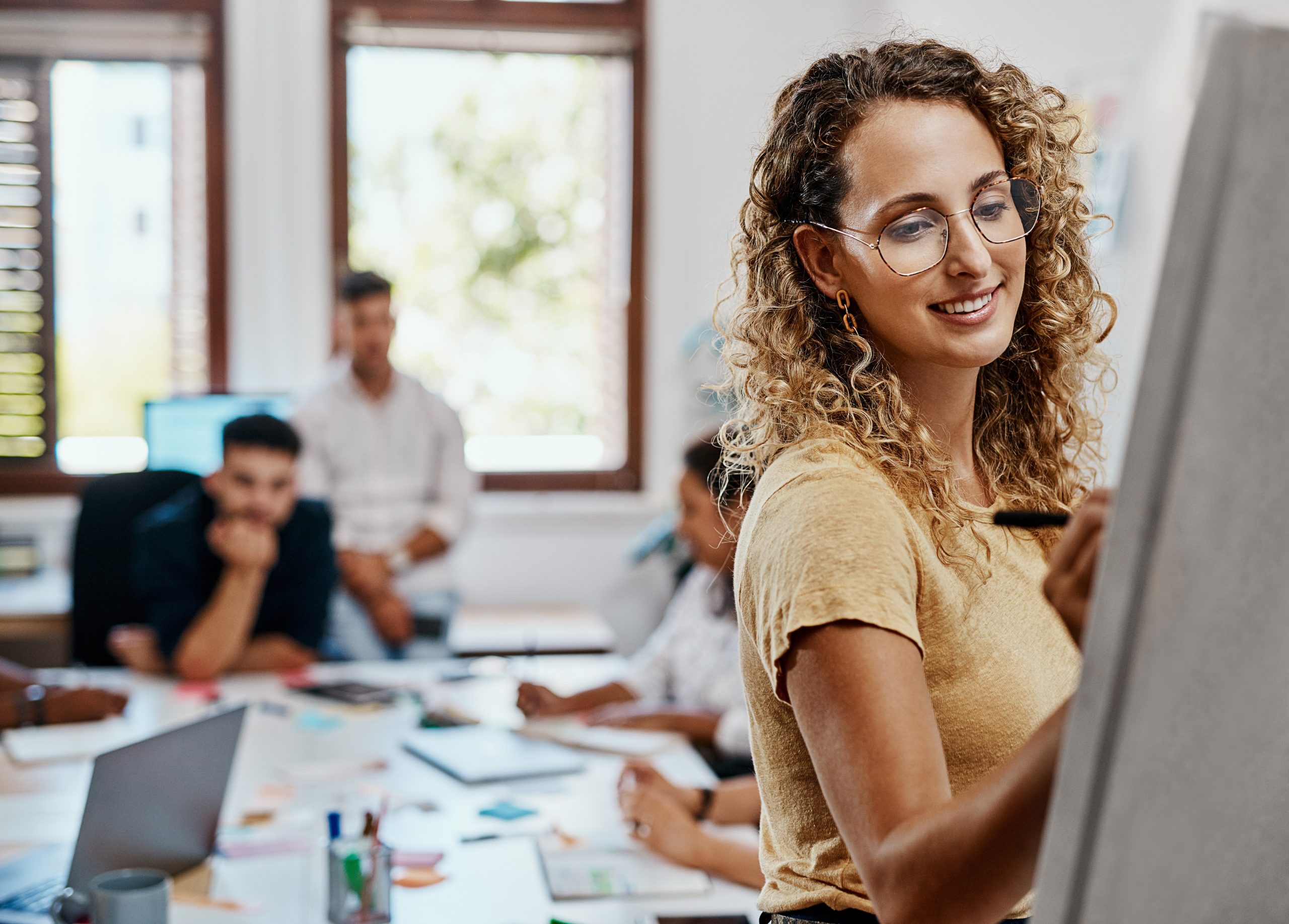 woman writing on board in a meeting with colleagues